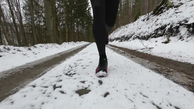 Close up front view of a trail runner on wintery forest trails on snow. Shoes are red and the runner applies a forefoot or midfoot strike.