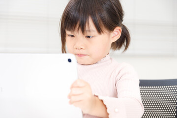 タブレット端末を使って真剣に勉強またはゲームをする女児