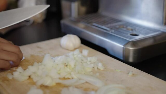 Onion skins, chilis, spices and brown woman's hands dicing onions. Handheld pan.