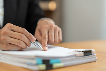 Financial advisor, analyst, asian businesswoman pointing at financial statistics report paper business income Taxes piled up on the desk to validate presentations at office meetings.