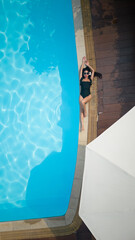 A girl in swimwear with sunglasses is lying at a swimming pooll edge smiling looking at the camera