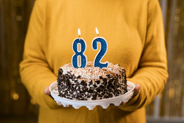 Woman holding a festive cake with number 82 candles while celebrating birthday party. Birthday...