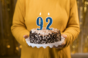 Happy birthday. Woman holding fresh delicious birthday cake with burning candle number 92, close up. Celebration of birthday at home.