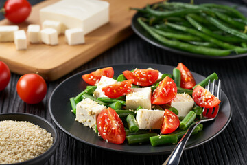 greek green beans and  tomato, herbs and olive oil on white plate served with feta cheese.