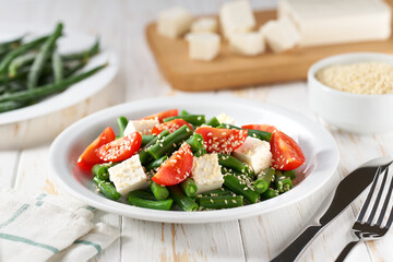 Fresh summer green beans salad bowl with tomatoes, feta, and sesame. Plate with delicious green beans salad on wooden table, closeup