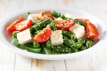 Green beans salad with feta on a white plate. Green beans and tomato salad on white plate.