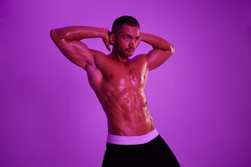 Fototapeta premium Man athletic body bodybuilder in briefs with nude torso abs full-length in the background fitness classes, purple colored light. Advertising, sports, active lifestyle, competition, challenge concept. 
