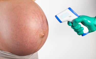 The doctor measures the temperature of the abdomen of a pregnant woman with an electronic...