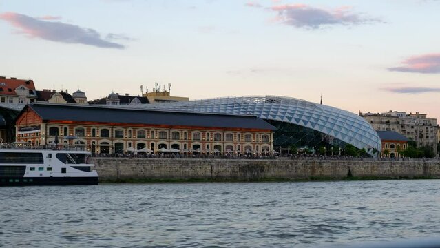 B&aacute;lna Shopping Mall on the Danube River in Budapest, Hungary. Ships, ferries, boats, cars, and tourists travel by. Beautiful evening golden hour sky with wispy clouds. Smooth 4k cinematic footage.