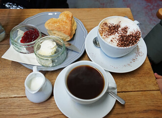 Close up scone with strawberry jam and clotted curd cream served with hot black coffee and Latte