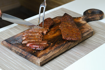 Cutting steak on wooden cutting board with knife and fork