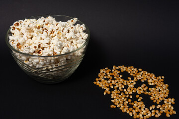 A bowl of fried popcorn and corn kernels on a black background