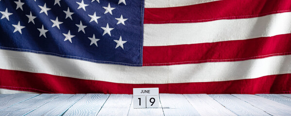 Small Wooden Calendar with Juneteenth 19 June on Wooden Countertop with American Flag