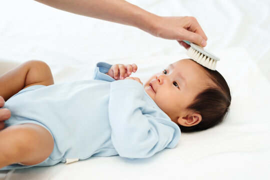 mother combing her newborn baby hair on bed