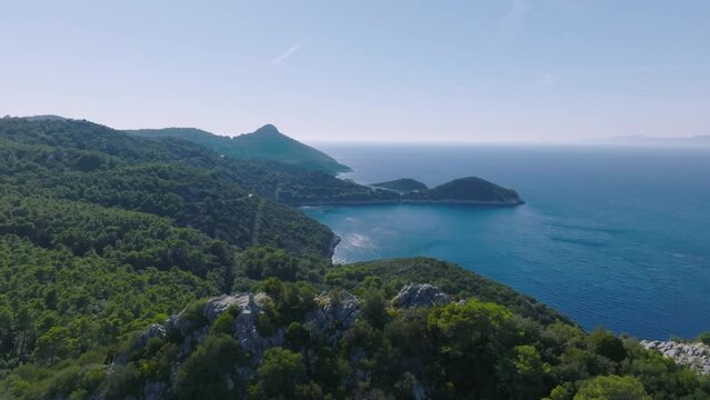 Aerial arc shot gently flying around the coastline of Lastovo Island, Croatia on a bright morning.