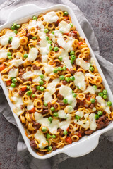 Anelli al Forno pasta baked with mince, vegetable and cheese closeup in a baking dish on the table. Vertical top view from above