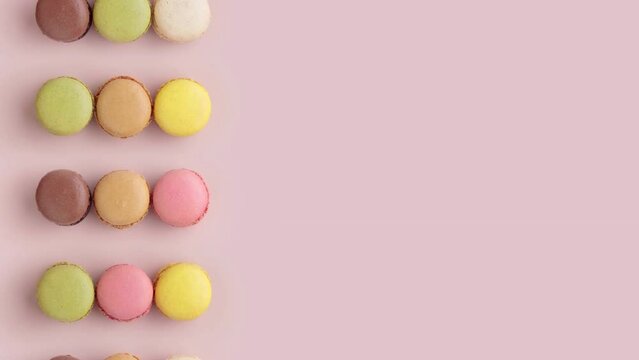 Colorful macaroons on pink background, top view video of moving rows, horizontal stop motion animation