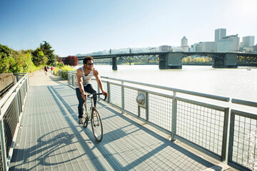 Young man cycling on promenade by river in city