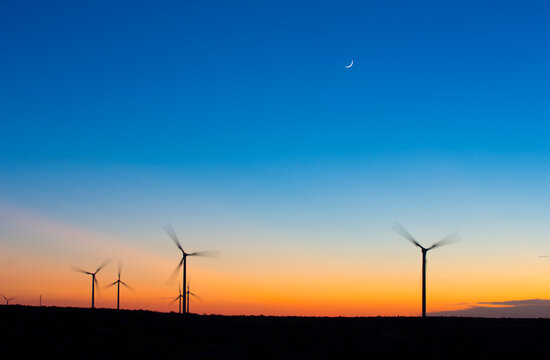 Silhouette wind turbines spinning against blue sky during sunset