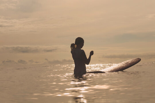 Silhouette woman with surfboard standing in sea