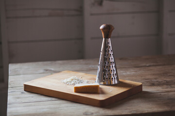 Cheese with grater on cutting board over wooden table