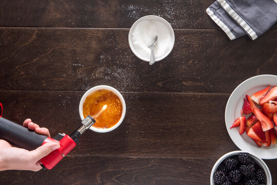 Cropped image of hand using butane torch while making creme brulee at table