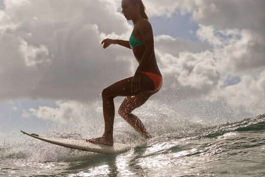 Low angle view of woman surfboarding in sea against cloudy sky