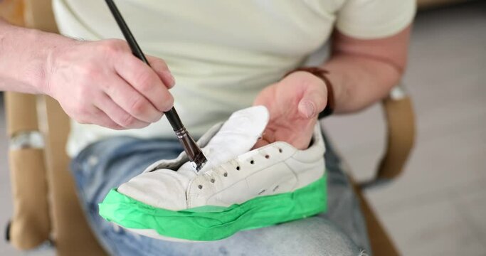 Master repairman painting sneakers with white paint in workshop closeup 4k movie slow motion