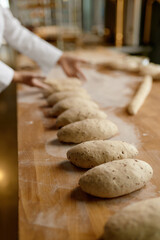 Baker working in bakery, forming baguettes from raw dough