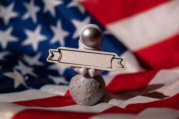 Plastic toy figure astronaut with paper note for your text on American flag background Copy space....