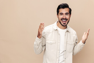 Portrait of a stylish man smile with teeth and surprise raised his hands with fists up on a beige background in a white t-shirt, fashionable clothing style, copy space, space for text