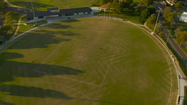 Friends practicing kicking Australian Rules Football on football oval.