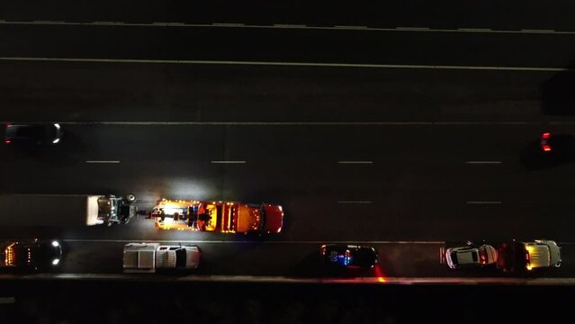 Bird's eye view of towing service pulling a truck and stopping in stop lane on the highway at night