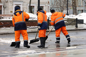 Three men workers clean snow with a shovels, snow removal in city. Early spring weather, street...