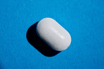Pharmacy healthcare concept. Close up of white drug capsule on blue background.