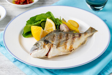 Grilled sea bream with vegetables and greens on wooden table