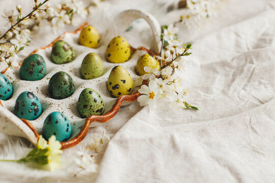 Rustic easter still life. Stylish easter eggs and blooming spring flowers on linen fabric. Happy Easter! Natural painted quail eggs in tray, feathers and cherry blossoms on rural table