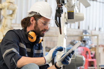 Male engineer worker working with tablet for control welding robot arm in workshop. Male engineer...