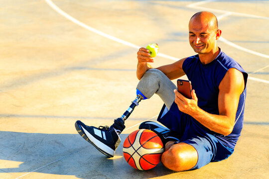 man with leg prosthesis playing basketball in tropical sea side at sumset time eating an apple - Powered by Adobe