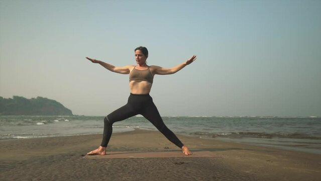 Warrior 2 yoga pose being completed in slow mo by teacher on coastline.