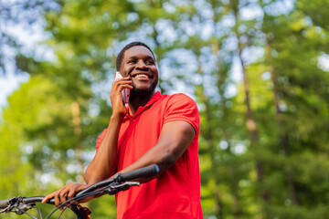 afro american man in red t-shirt walking in park with a bicycle