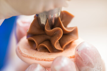 the pastry chef squeezes the filling onto macarons cookies. close-up. home bakery concept.