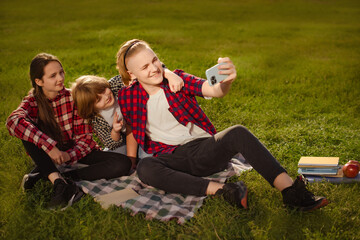 two boys brothers with girl sister make selfie on phone on green grass in summer picnic ourdoors