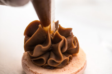 the pastry chef squeezes the filling onto macarons cookies. close-up. home bakery concept.
