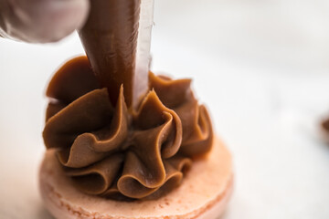 the pastry chef squeezes the filling onto macarons cookies. close-up. home bakery concept.