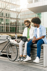 Young freelancers working together on laptop sitting outdoors next to bicycle