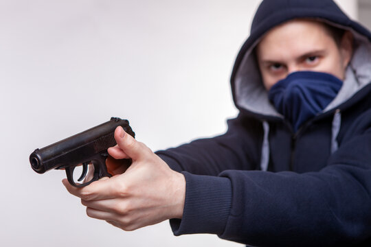 Hooded man holds hand gun and points it to the camera. Concept of crime and fire arm assault with mature man. Armed robbery on black, shallow depth of field, focus on the barrel of the pistol.