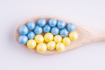 Blue and yellow balls in a wooden spoon on a white background
