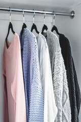 minimalist capsule wardrobe selection of womenswear sweaters and cardigans with matching hangers shot at shallow depth of field