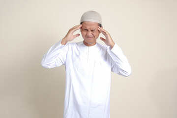 Portrait of attractive Asian muslim man in white shirt having a migraine, touching his temple....